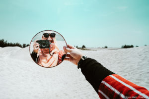 girl holding mirror and she is in the mirror holding a camera