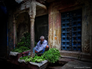 man sitting under an overhang laying out fruits and vegetables