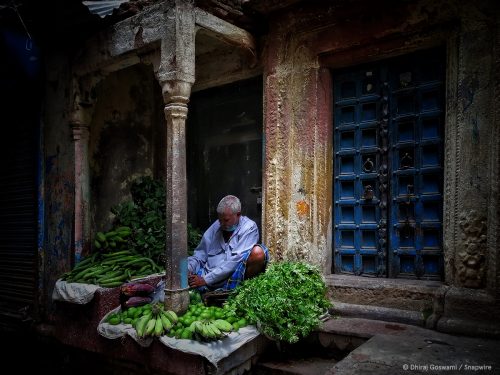 man sitting under an overhang laying out fruits and vegetables