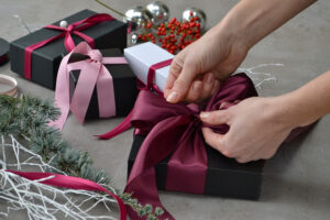 female tying burgundy bow on present