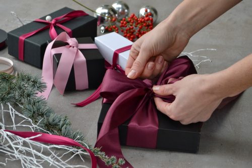 female tying burgundy bow on present