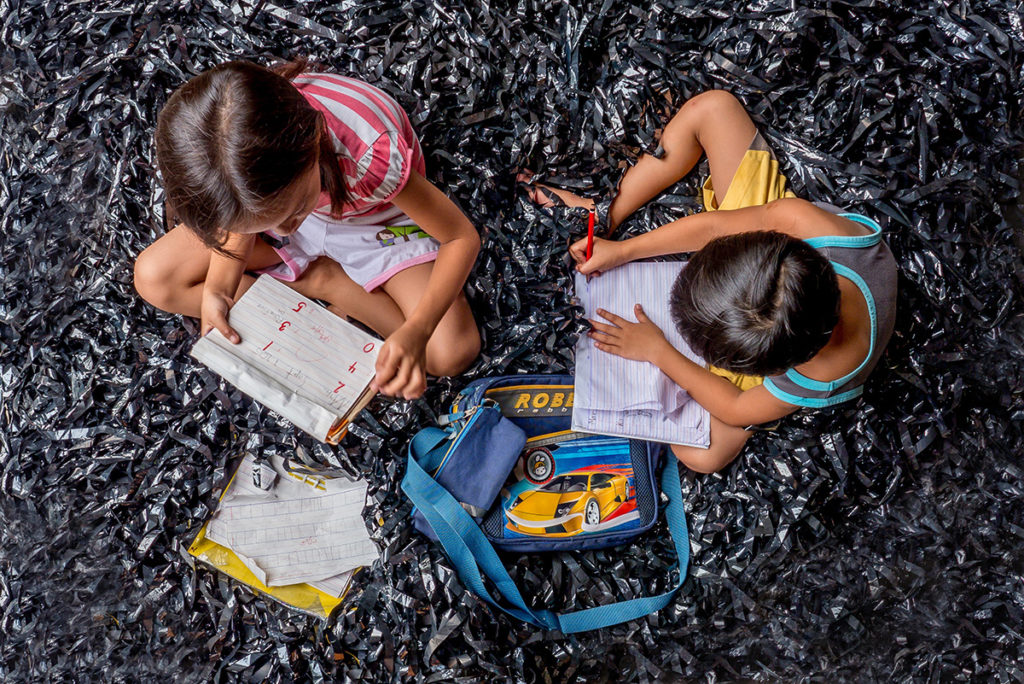 two kids writing in a book on a carpet