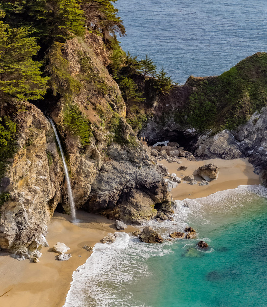 birds eye shot of a cove with a waterfall going into the ocean