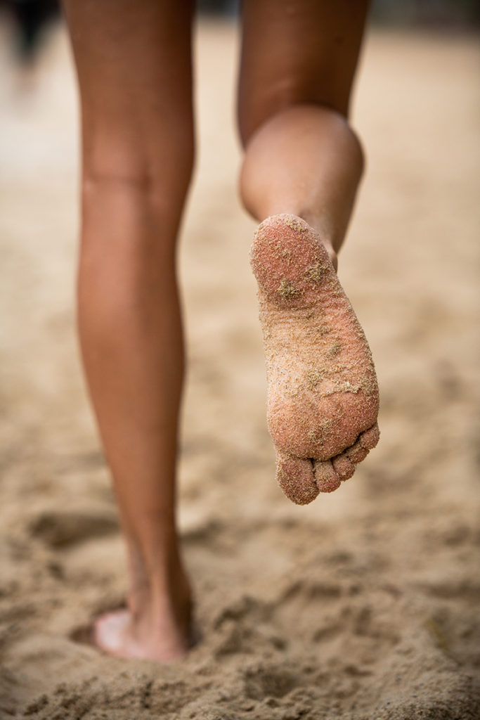 picture of someones feet from behind as they walk on the beach 