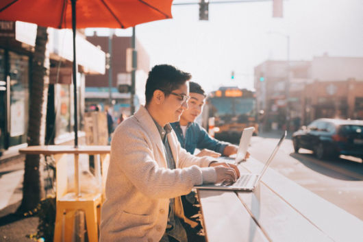 two guys working on laptops outside